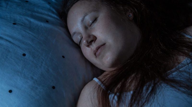 Personne endormie paisiblement sur un oreiller dans une chambre sombre, illustrant le sommeil réparateur et les bienfaits du repos nocturne sur la santé physique et mentale.