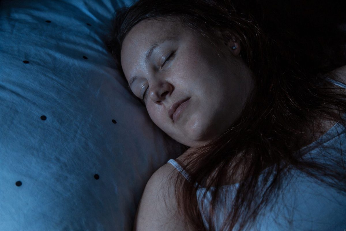 Personne endormie paisiblement sur un oreiller dans une chambre sombre, illustrant le sommeil réparateur et les bienfaits du repos nocturne sur la santé physique et mentale.