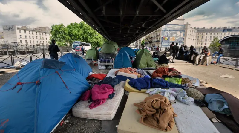 campement de tentes installé dans une rue urbaine étroite avec plusieurs personnes vivant sur place et des affaires personnelles visibles illustrant la précarité en ville