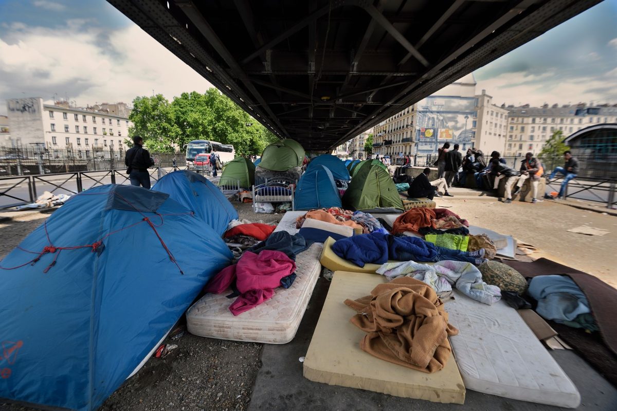 campement de tentes installé dans une rue urbaine étroite avec plusieurs personnes vivant sur place et des affaires personnelles visibles illustrant la précarité en ville