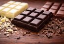 Tablettes de chocolat noir, chocolat au lait et chocolat blanc disposées côte à côte sur une surface en bois, avec le chocolat noir au centre en premier plan, illustrant la différence de couleur, de texture et de composition nutritionnelle entre les trois types de chocolat.