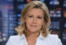 présentatrice de journal télévisé blonde assise sur un plateau de télévision avec écrans lumineux flous en arrière-plan, regard calme face caméra
