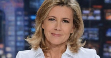 présentatrice de journal télévisé blonde assise sur un plateau de télévision avec écrans lumineux flous en arrière-plan, regard calme face caméra