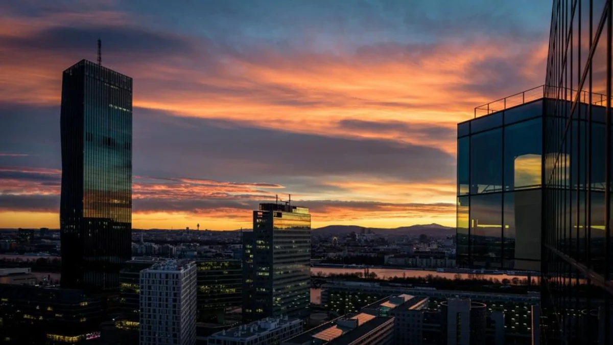 Panorama d’une grande ville moderne au coucher du soleil avec plusieurs gratte-ciel en verre et en acier dominant l’horizon, ciel orange et violet au-dessus d’un fleuve et d’un quartier d’affaires dense, illustrant un centre financier international associé à l’expatriation économique et aux stratégies d’optimisation fiscale.