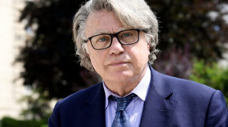 Portrait d’un homme en costume et lunettes au regard sérieux, sur fond extérieur flou, illustrant une polémique liée à une fake news virale diffusée sur les réseaux sociaux.