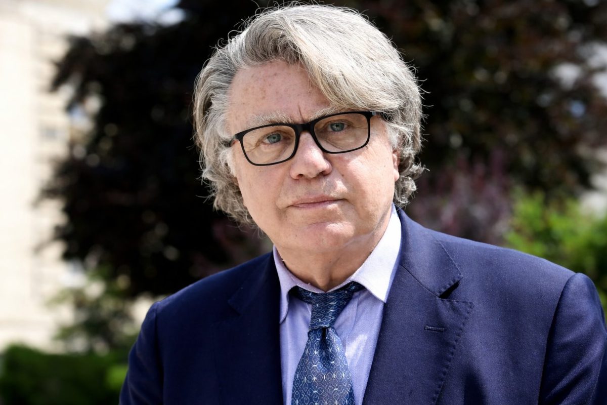 Portrait d’un homme en costume et lunettes au regard sérieux, sur fond extérieur flou, illustrant une polémique liée à une fake news virale diffusée sur les réseaux sociaux.