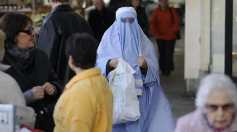 femme portant un voile intégral marchant dans une rue commerçante animée d’une ville européenne parmi des passants