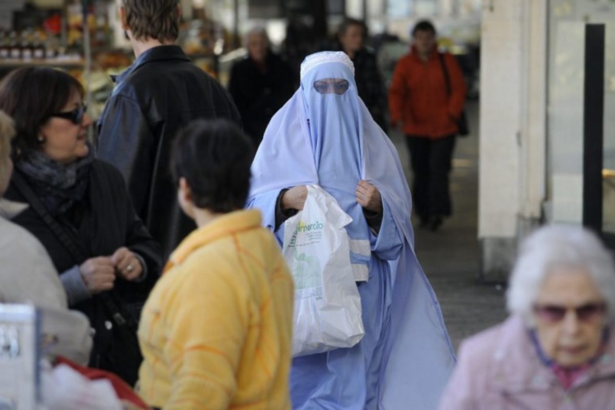 femme portant un voile intégral marchant dans une rue commerçante animée d’une ville européenne parmi des passants