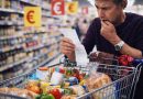 homme inquiet dans un supermarché regardant un long ticket de caisse avec un caddie rempli de produits alimentaires illustrant la hausse des prix et l’inflation sur les courses du quotidien