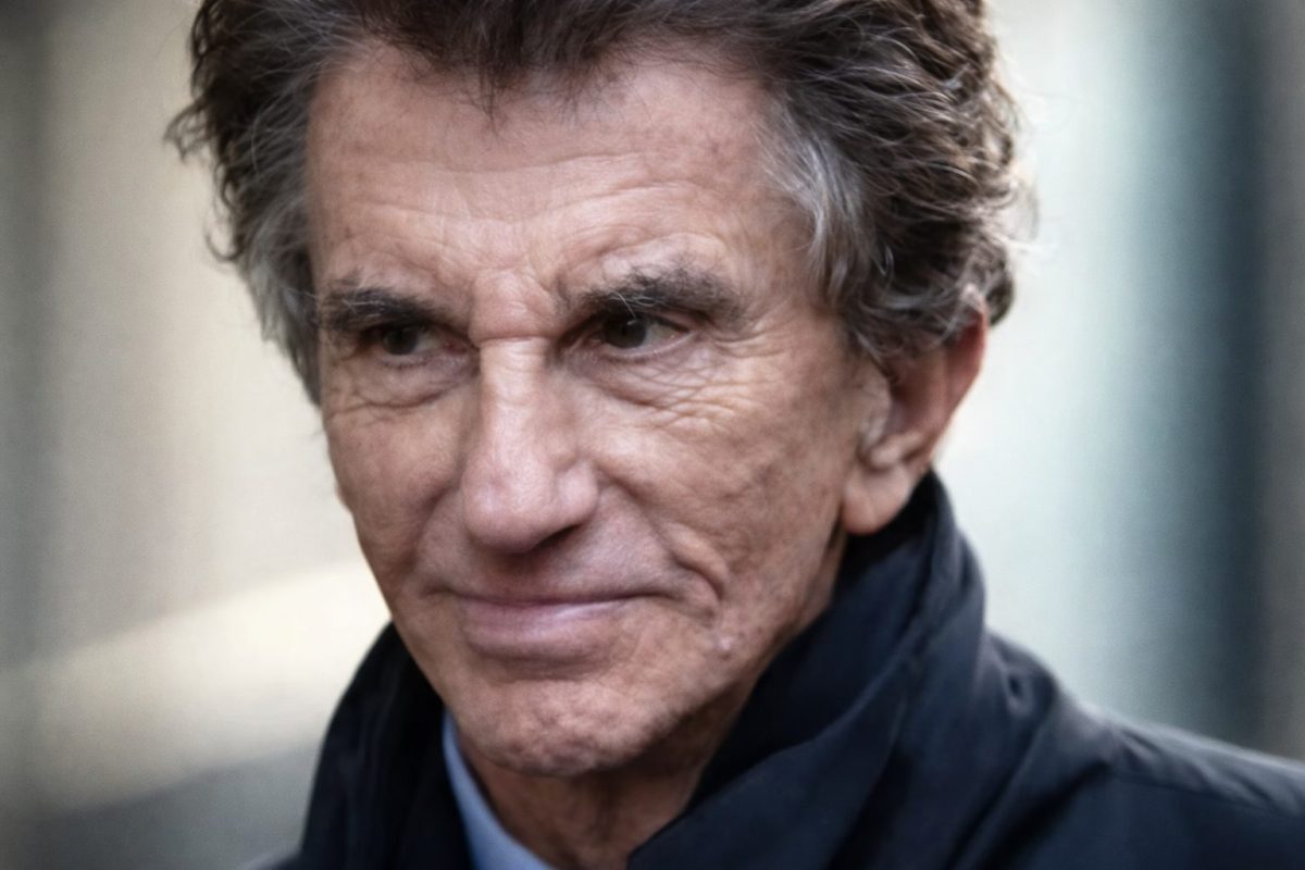 Gros plan sur le visage d’un homme âgé au regard intense et fermé, expression tendue, avec des rides marquées et un fond urbain flou en arrière-plan