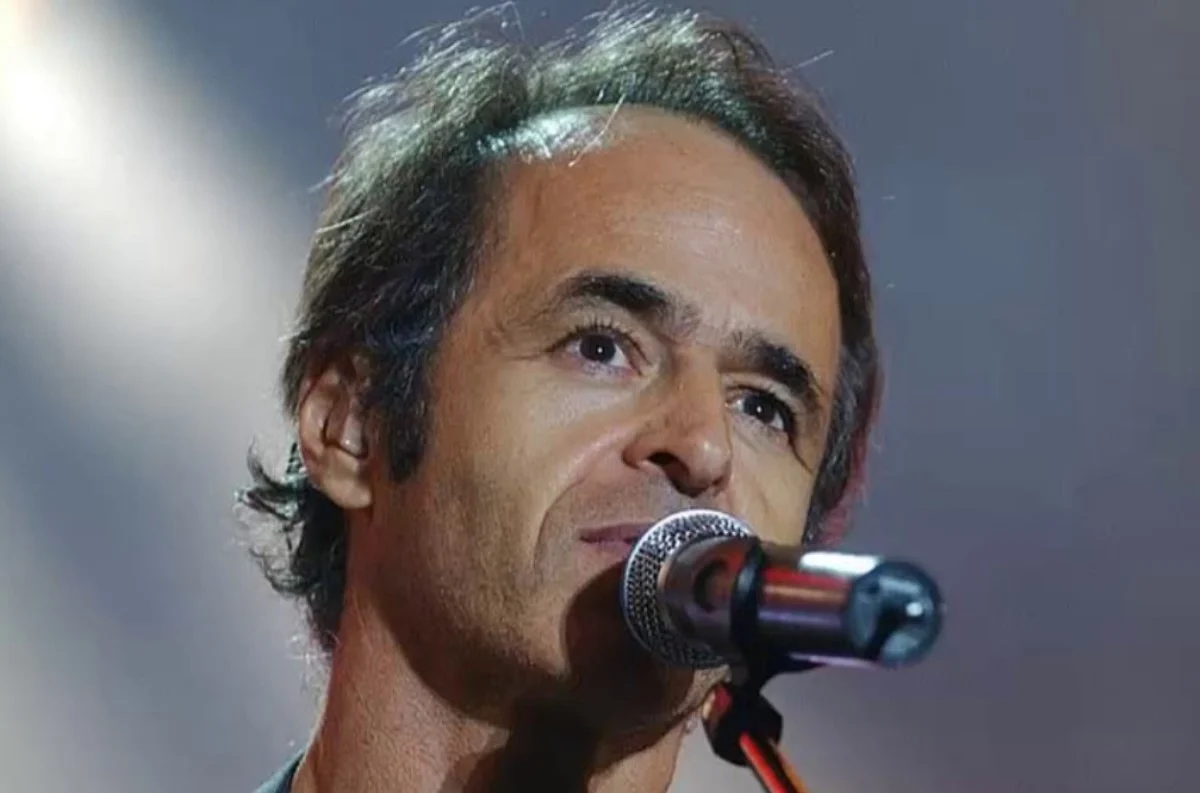 Portrait d’un chanteur français célèbre sur scène, micro à la main, regard concentré sous les projecteurs, illustrant l’univers musical et la discrétion de sa vie familiale évoquée dans un témoignage de son fils.