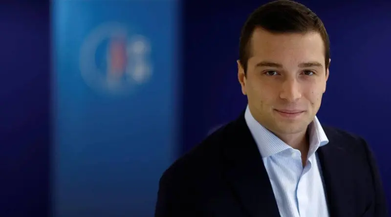 portrait d’un homme politique français en costume sombre regardant l’objectif devant un fond bleu institutionnel dans un cadre officiel