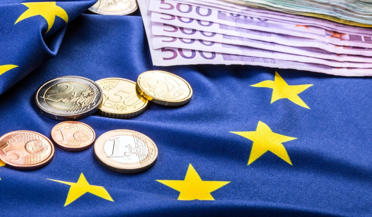 Billets et pièces en euros posés sur un drapeau bleu avec des étoiles jaunes symbolisant l’Union européenne, illustrant l’épargne, la monnaie européenne et les questions financières liées aux comptes d’épargne et à l’argent des particuliers.