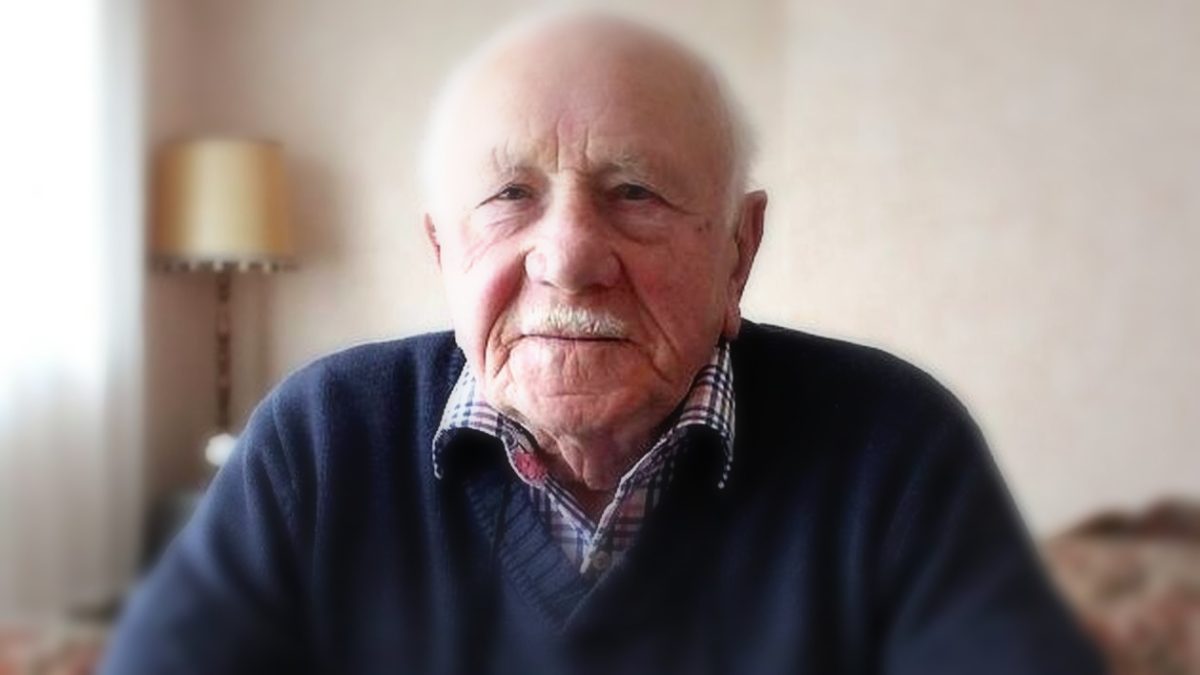 Portrait d’un homme âgé au regard sérieux, représentant un élu local expérimenté, assis en intérieur avec un arrière-plan flou mettant en valeur son visage marqué par le temps