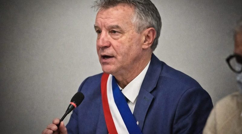 Homme politique portant une écharpe tricolore parlant au micro lors d’une réunion officielle, regard sérieux, cadrage serré sur le visage, ambiance institutionnelle tendue