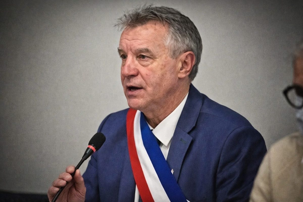 Homme politique portant une écharpe tricolore parlant au micro lors d’une réunion officielle, regard sérieux, cadrage serré sur le visage, ambiance institutionnelle tendue