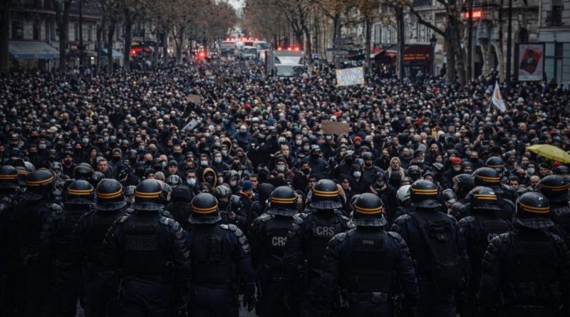 Foule dense de manifestants rassemblés dans une large avenue urbaine, faisant face à une ligne compacte de policiers en tenue antiémeute, casques et équipements de maintien de l’ordre visibles, créant une scène de confrontation directe dans une ambiance tendue et dramatique.