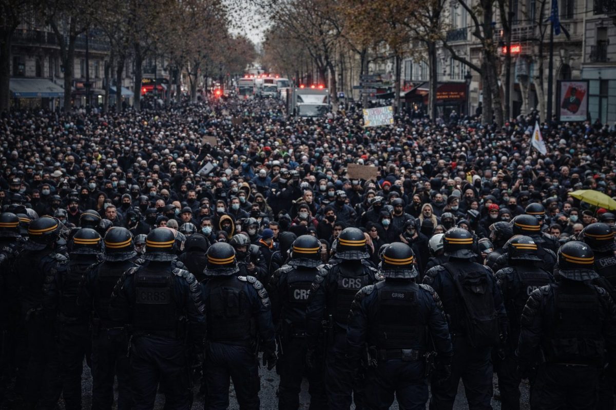 Foule dense de manifestants rassemblés dans une large avenue urbaine, faisant face à une ligne compacte de policiers en tenue antiémeute, casques et équipements de maintien de l’ordre visibles, créant une scène de confrontation directe dans une ambiance tendue et dramatique.