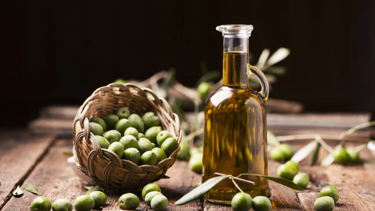 Huile d’olive vierge extra dans une bouteille en verre posée sur une table en bois avec des olives vertes fraîches dans un panier, éclairage naturel chaleureux en cuisine