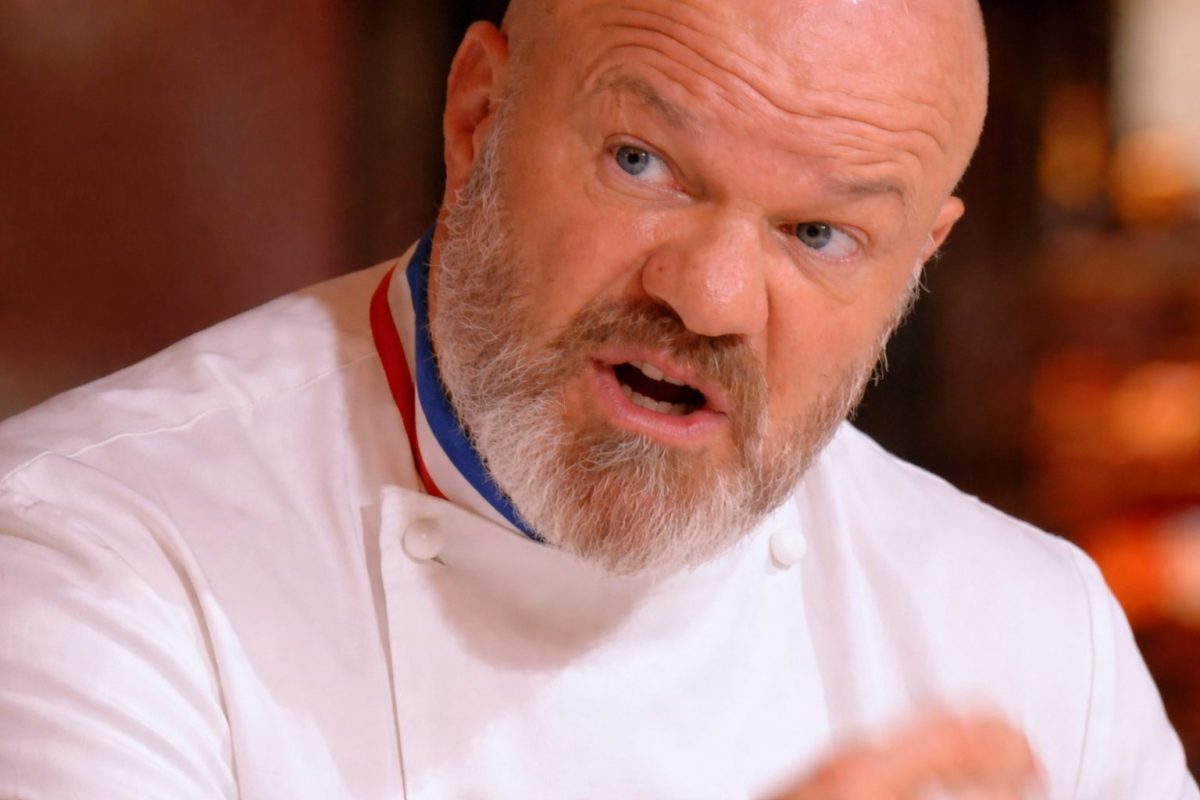 chef cuisinier en veste blanche parlant avec intensité dans une salle de restaurant pendant un moment de tension avec des clients
