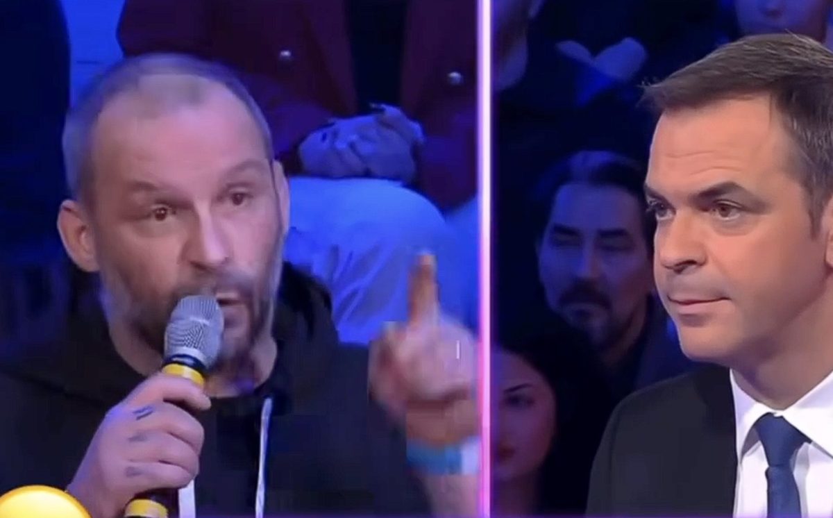 Un restaurateur s’exprime avec émotion en tenant un micro sur un plateau de télévision, pointant le doigt pour appuyer ses propos, face à un ancien ministre en costume qui l’écoute attentivement lors d’un débat sur la pression fiscale et les difficultés financières des entrepreneurs.