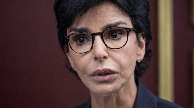 Portrait en gros plan d’une femme politique au regard intense, visage tendu et lunettes, dans un contexte de forte tension médiatique