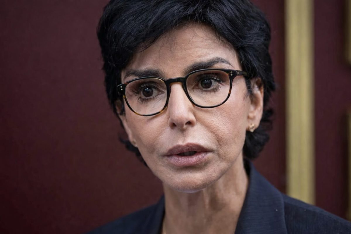 Portrait en gros plan d’une femme politique au regard intense, visage tendu et lunettes, dans un contexte de forte tension médiatique