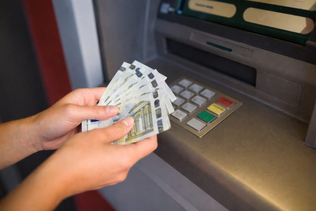mains tenant plusieurs billets en euros devant un distributeur automatique lors d’un retrait d’argent, clavier et écran visibles, ambiance réaliste illustrant une opération bancaire et un possible détournement de fonds