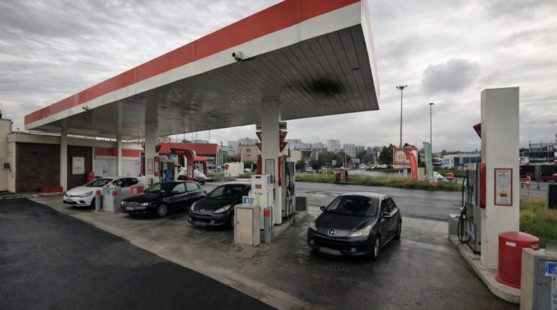 station-service avec plusieurs voitures faisant le plein de carburant sous un ciel gris dans un contexte de hausse des prix de l’essence