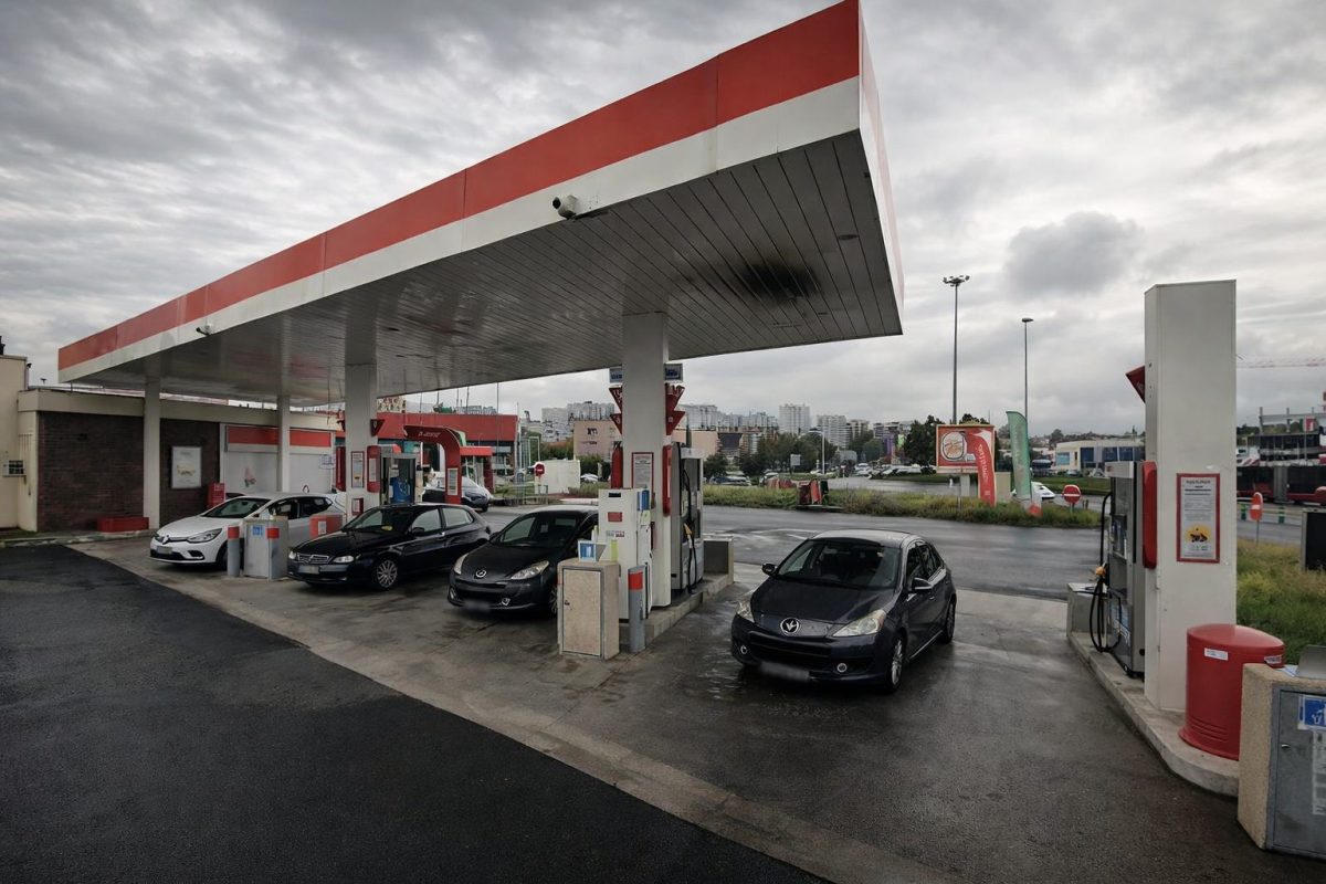 station-service avec plusieurs voitures faisant le plein de carburant sous un ciel gris dans un contexte de hausse des prix de l’essence