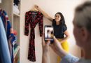 personne photographiant une robe suspendue sur un cintre avec un smartphone pour la vendre sur une application de vêtements d’occasion, dans une pièce avec une armoire remplie de vêtements