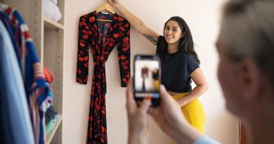 personne photographiant une robe suspendue sur un cintre avec un smartphone pour la vendre sur une application de vêtements d’occasion, dans une pièce avec une armoire remplie de vêtements