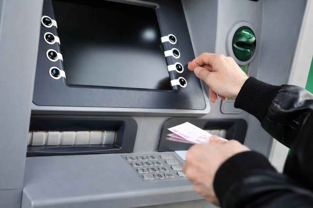 main d’un homme retirant de l’argent à un distributeur automatique avec une carte bancaire, écran flouté, ambiance neutre illustrant un retrait suspect et une possible fraude bancaire