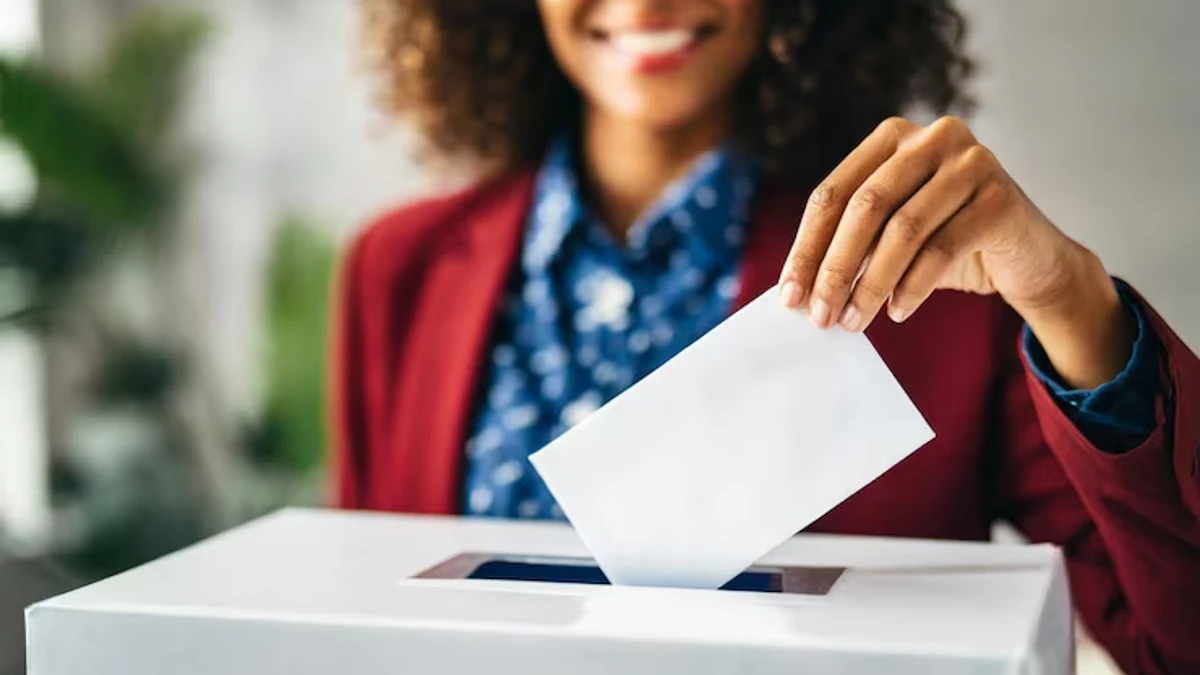 Main d’une femme déposant un bulletin blanc dans une urne électorale lors d’un vote, gros plan sur le geste avec une urne blanche au premier plan et un arrière-plan flou montrant une personne souriante, scène symbolisant la participation démocratique et le processus électoral