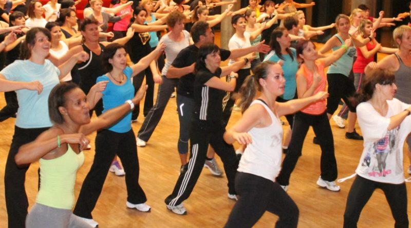 Groupe de participants en plein cours d’aérobic collectif réalisant des mouvements dynamiques et synchronisés en musique dans une salle de fitness lumineuse