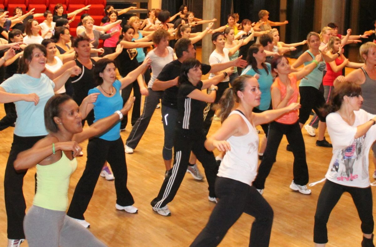 Groupe de participants en plein cours d’aérobic collectif réalisant des mouvements dynamiques et synchronisés en musique dans une salle de fitness lumineuse