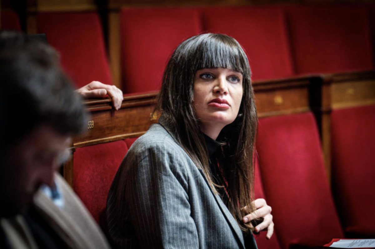 Femme politique assise sur un banc rouge dans une assemblée, regard attentif et posture sérieuse, illustrant un débat politique et la représentation à l’Assemblée nationale
