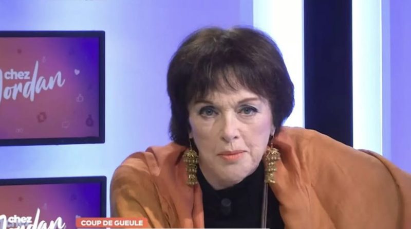 Femme en plateau télévisé regardant la caméra avec une expression sérieuse, éclairage studio, ambiance débat, décor coloré avec écrans en arrière-plan