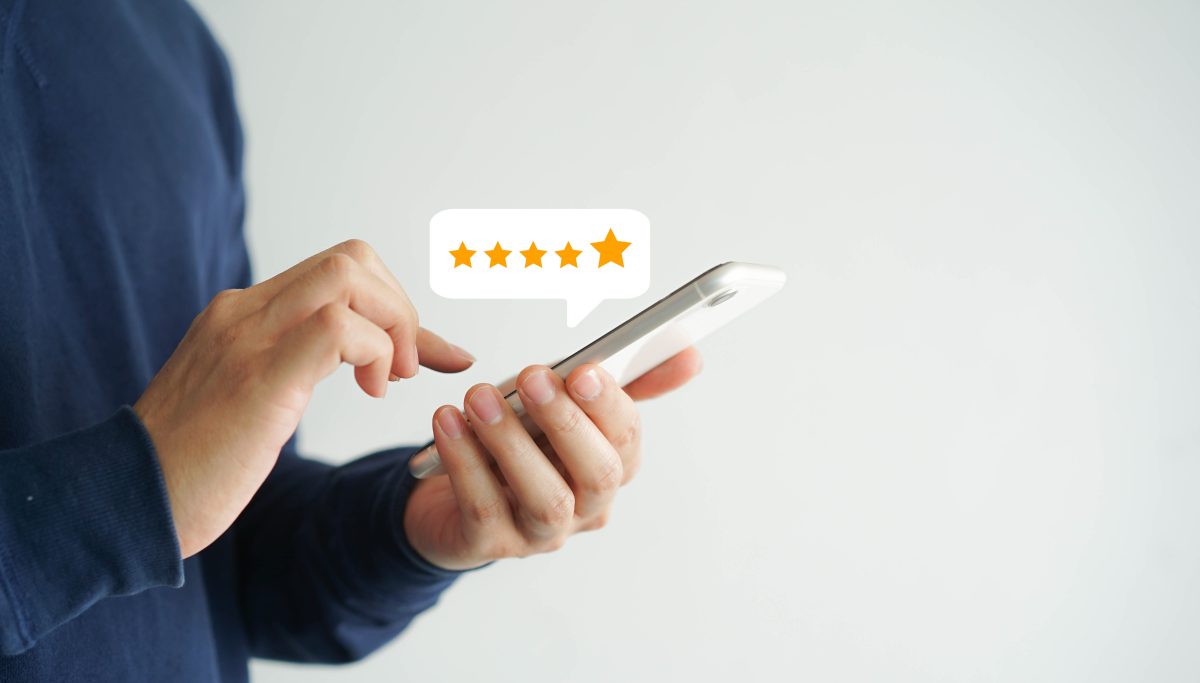 Personne tenant un smartphone et laissant un avis en ligne avec des étoiles visibles à l’écran, illustrant la publication de commentaires sur internet et les risques liés aux avis négatifs et à la diffamation