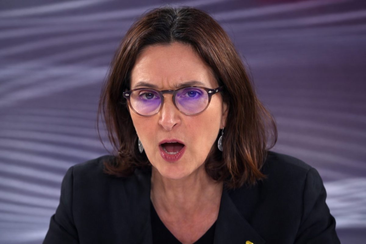 Femme en plateau télévisé, visage tendu et bouche entrouverte, regard intense derrière des lunettes, exprimant colère et tension lors d’une prise de parole médiatique