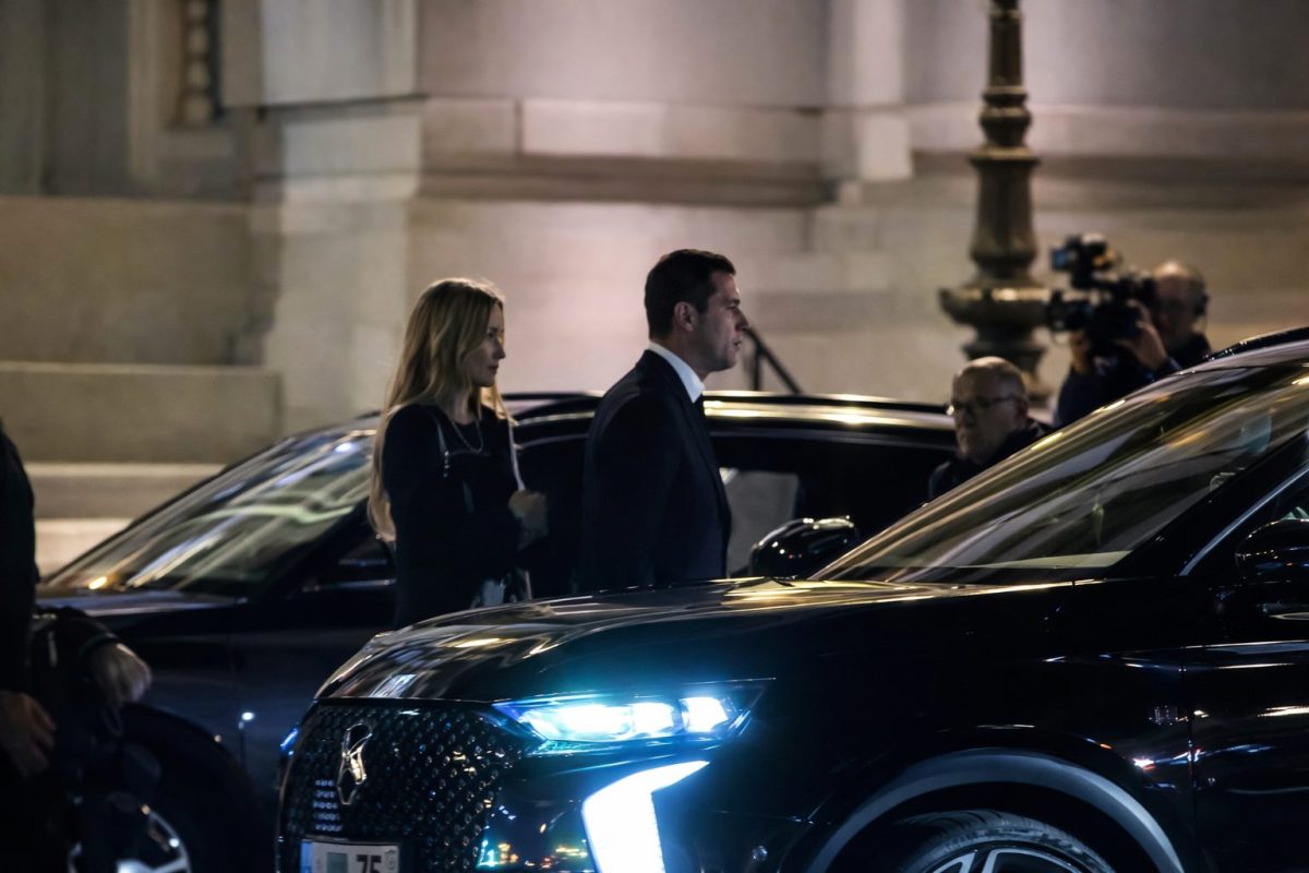 Couple marchant de nuit à proximité d’une voiture sombre avec phares allumés, ambiance tendue suggérant une surveillance discrète dans un contexte urbain élégant