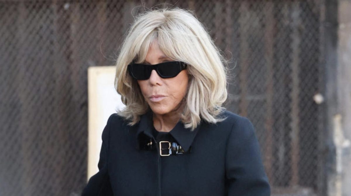 Portrait d’une femme aux cheveux blonds portant des lunettes noires et un manteau sombre, affichant une expression fermée lors d’un déplacement officiel