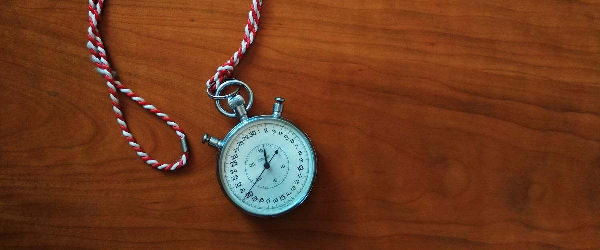 Chronomètre posé sur une surface en bois avec cordon rouge et blanc, illustrant la gestion du temps, la ponctualité et la mesure des secondes
