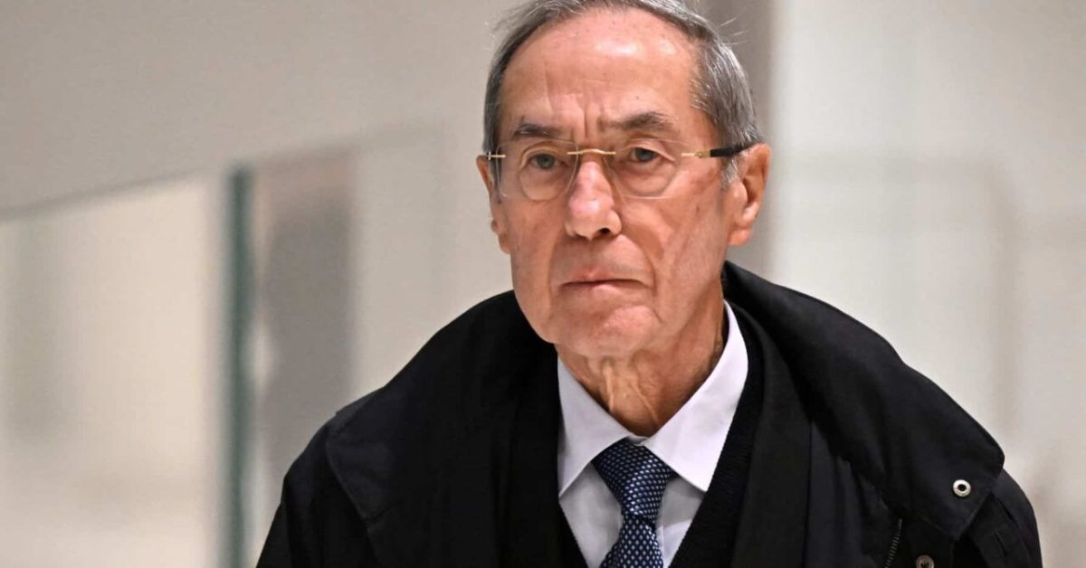 Homme âgé au visage marqué et sérieux, portant des lunettes et un costume sombre, regard déterminé dans un environnement institutionnel évoquant un contexte judiciaire et une forte tension