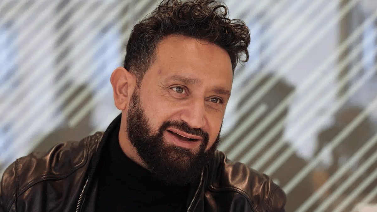 Animateur de télévision français barbu souriant lors d’une interview, vêtu d’une veste en cuir, regard tourné vers son interlocuteur dans un décor intérieur moderne