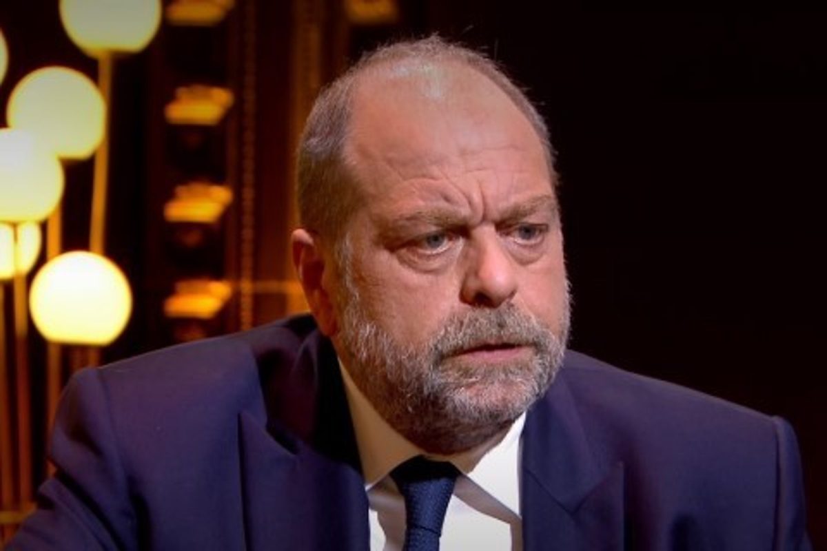 Homme assis sur un plateau de télévision, visage fermé et regard intense, exprimant une émotion contenue dans une ambiance chaleureuse avec éclairage tamisé en arrière-plan