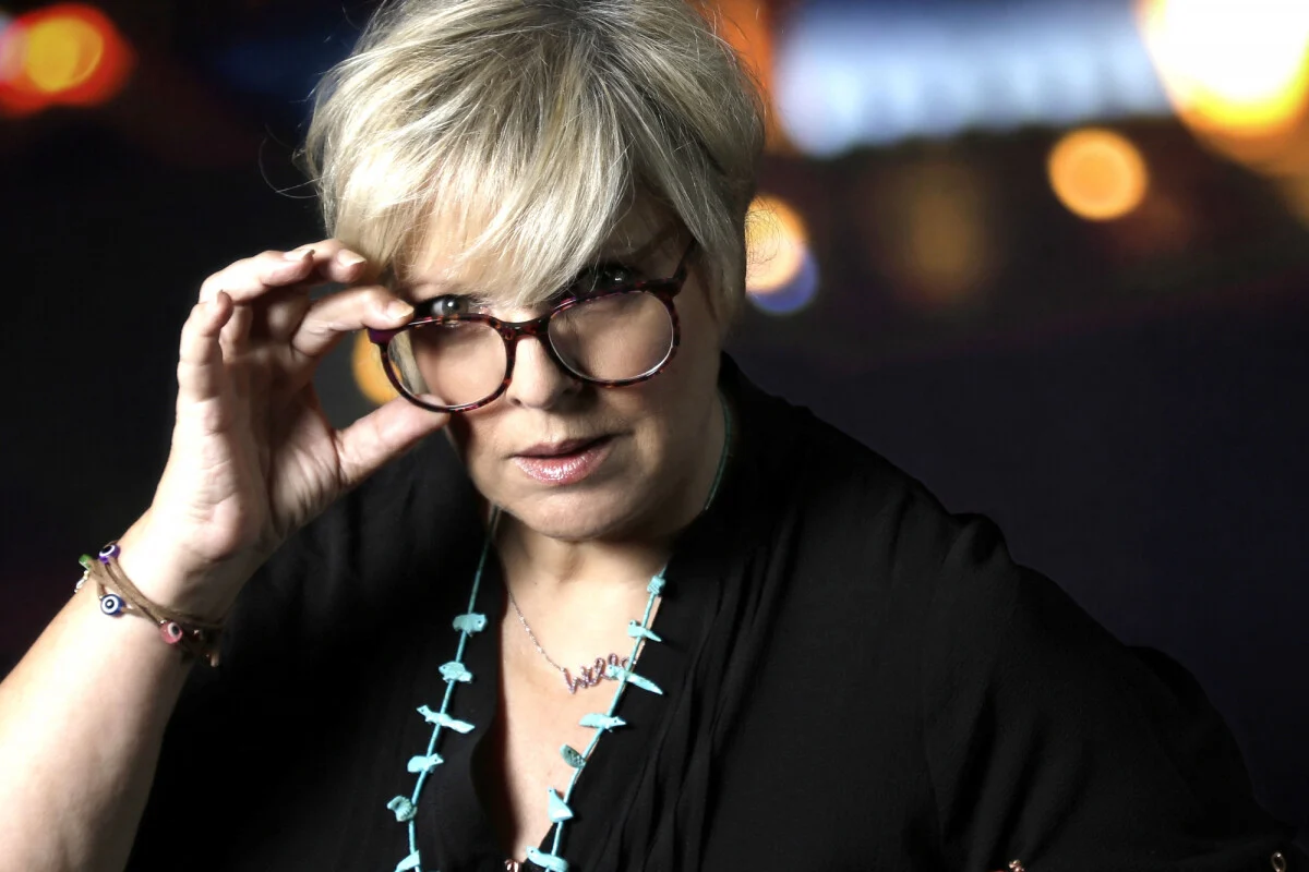 Femme blonde aux cheveux courts ajustant ses lunettes avec un regard intense, sur fond nocturne flou, illustrant un témoignage fort sur une relation toxique et des violences psychologiques