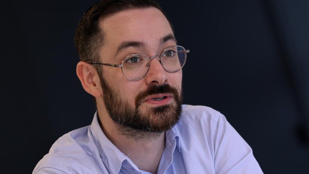 Portrait d’un homme politique barbu portant des lunettes, en train de s’exprimer lors d’un échange sérieux, illustrant une polémique liée à une décision municipale et à une hausse contestée d’indemnités