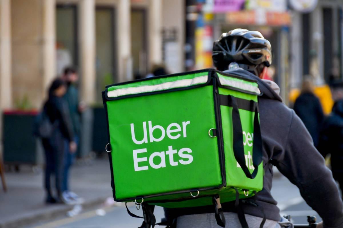 Livreur à vélo circulant en ville avec un grand sac isotherme vert de livraison sur le dos, symbole du travail précaire et intensif dans le secteur de la livraison à domicile en France