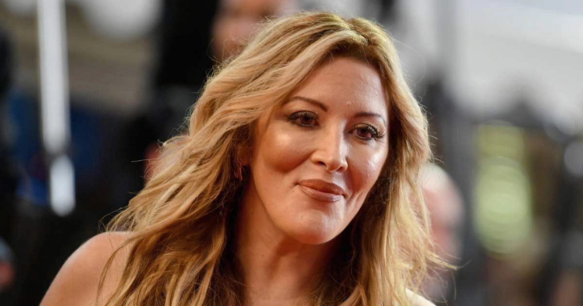 Portrait d’une femme blonde souriante lors d’un événement public, éclairage naturel, regard tourné légèrement sur le côté, ambiance médiatique
